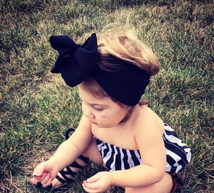 Toddler girl outfit featuring a black bow headband, striped top, and strappy sandals