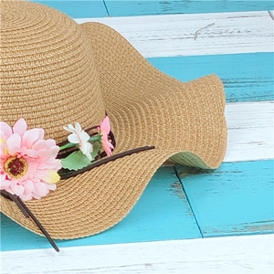 Summer straw sun hat with pink daisy trim and wavy brim on light blue wooden backdrop