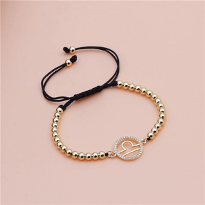 Detail of Libra zodiac charm on a black braided cord bracelet with gold beads