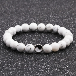 Detail of white marble stone beads with yin yang metal charm on textured black background