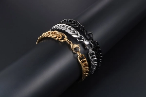 Detailed close-up of three Cuban link bracelets in gold, silver, and black metal finishes
