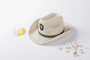 Detail of cream straw cowboy hat with ethnic band and bull emblem on summer beach props