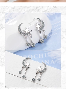 Detail of silver moon and star earrings with rhinestones on a white ceramic tray