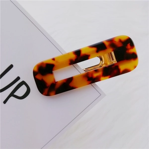Detail of a rectangular tortoiseshell hair clip with a gold metal spring on a white card