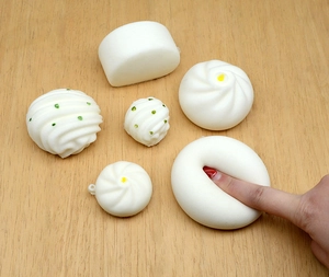 Detail showing hand pressing a soft slow rebound steamed bun squishy toy on wood