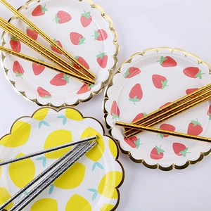 Close-up of strawberry and lemon paper plates with gold foil edges and matching straws