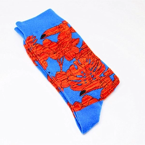 Close-up of bright blue cotton socks featuring orange tropical leaf patterns and knitting