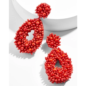 Detail of red beaded bohemian drop earrings featuring handmade teardrop design on white stand