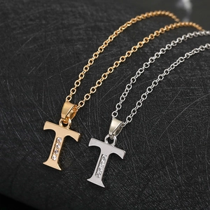 Close-up of gold and silver T-letter necklaces with inlaid zircon on black texture