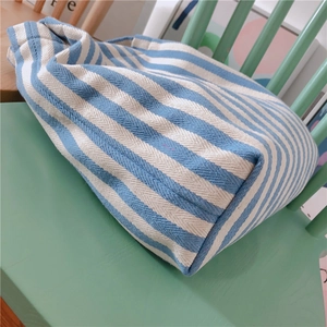 Close-up of blue and white striped canvas tote bag texture on a green wooden bench