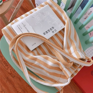Detail of yellow and white striped canvas tote bag on a green chair with a book