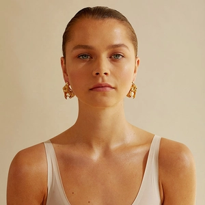 Detail view of gold floral irregular brass earrings with center white pearl on a model