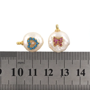 Detailed view of baroque pearl pendants with heart and butterfly micro-inlay next to a ruler