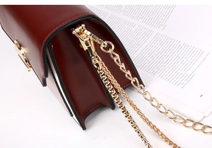 Detail of burgundy crossbody bag with triple-style golden chain and spring hook clasp