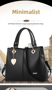 Detail view of black faux leather tote bag with gold heart pendant and metallic accents