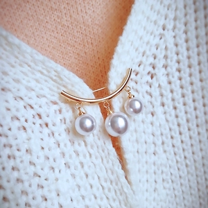 Detailed view of a gold-tone enamel snail brooch with white pearls on a white cardigan