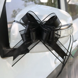 Dettaglio di un grande fiocco in organza nero sullo specchietto di un'auto bianca per nozze