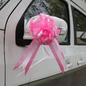 Close-up of a pink sphere bow ribbon flower with long streamers on a white car mirror