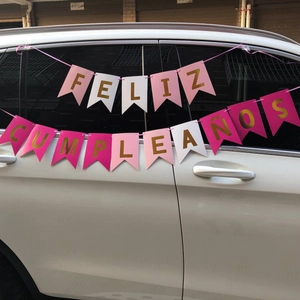 Pink Feliz Cumpleaños birthday banner with gold letters hung on a white car for outdoor use