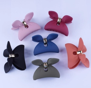 Flat lay of six large 12cm matte bow hair claws in various colors on purple background