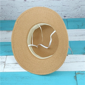Straw sun hat with white windproof cord and dotted ribbon on a wooden background
