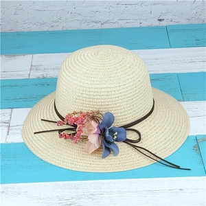Cappello di paglia da donna con decorazioni floreali su legno blu e muro di mattoni bianchi