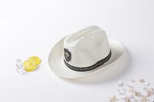 Detail of white straw cowboy hat with black woven band and metal shield badge on beach scene