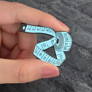 Detailed view of creative blue tape measure enamel brooch held in hand for scale