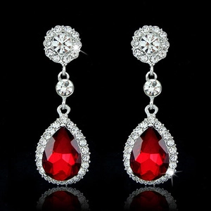 Macro view of teardrop red gemstone earrings with sparkling diamond halo and silver setting