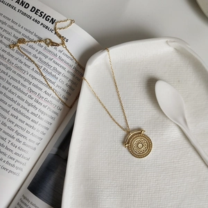 Close-up of golden S925 sterling silver round medallion pendant on white ceramic plate