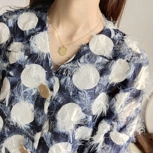 Detail of gold round pendant necklace worn with a textured blue white fringe tweed jacket