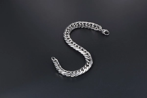 Macro shot of silver stainless steel Cuban link bracelet with lobster clasp on dark background