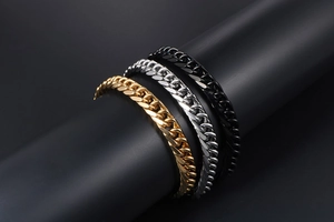 Close-up of three Cuban link bracelets in gold, silver, and black on a black stand