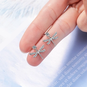 Sparkling dragonfly stud earrings in silver metal with rhinestones held on fingertips