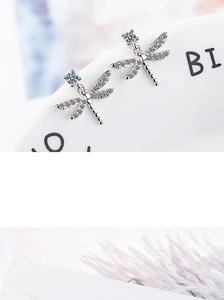 Detailed macro shot of silver dragonfly earrings with sparkling zircons on white ceramic