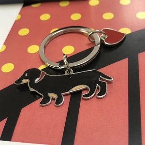 Close-up of black dachshund keychain with red heart charm on yellow polka dot background
