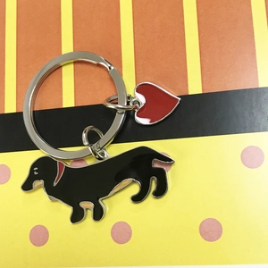 Detail view of a black dachshund metal keychain with red heart charm on a striped background