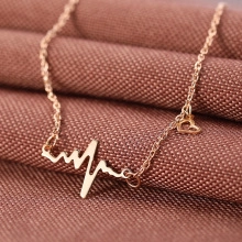 Macro shot of gold heartbeat pendant necklace with small heart on textured fabric