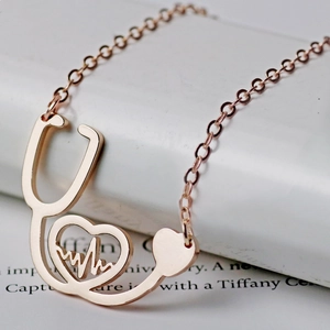 Rose gold stethoscope necklace with heart and heartbeat pendant on a book background