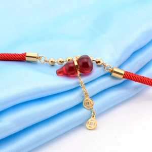 Dettaglio del bracciale in corda rossa con ciondolo a zucca traslucida e ciondoli dorati
