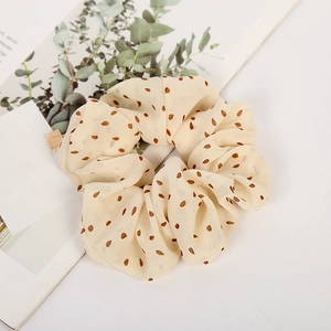 Elegant beige chiffon polka dot hair scrunchie styled on a magazine with eucalyptus leaves