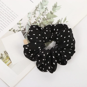 Black polka dot scrunchie with white dots on a bright lifestyle background with leaves