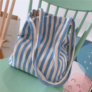 Detail of blue and white striped canvas tote bag resting on a light green wooden chair