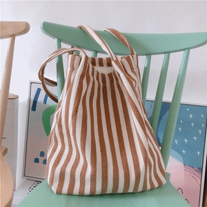 Minimalist brown and white vertical striped canvas shoulder bag hanging on a green chair