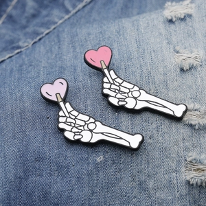 Cartoon skeleton hand heart enamel pins on blue denim fabric in pink and purple