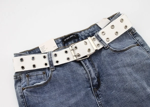 Detail of white double grommet canvas belt styled on blue denim jeans waist