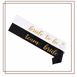 Close-up of white 'bride to be' and black 'team bride' satin sashes with gold foil lettering