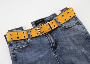 Detail of yellow canvas belt with double silver eyelets and twin-pin metal buckle