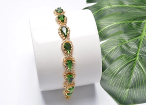Détail d'un bracelet doré avec cristaux verts poire sur un support d'exposition blanc