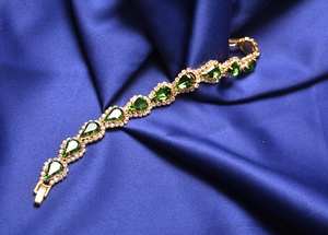 Détail du bracelet doré avec gemmes vertes en goutte et cristaux sur soie bleue